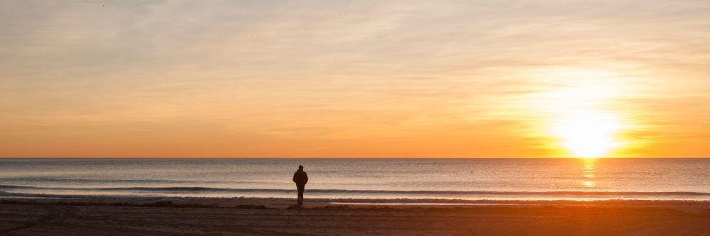 photo of a man on a beach watching the sunset