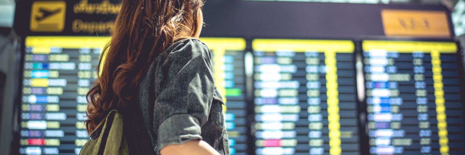 Photo of a woman standing before a flight departure screen