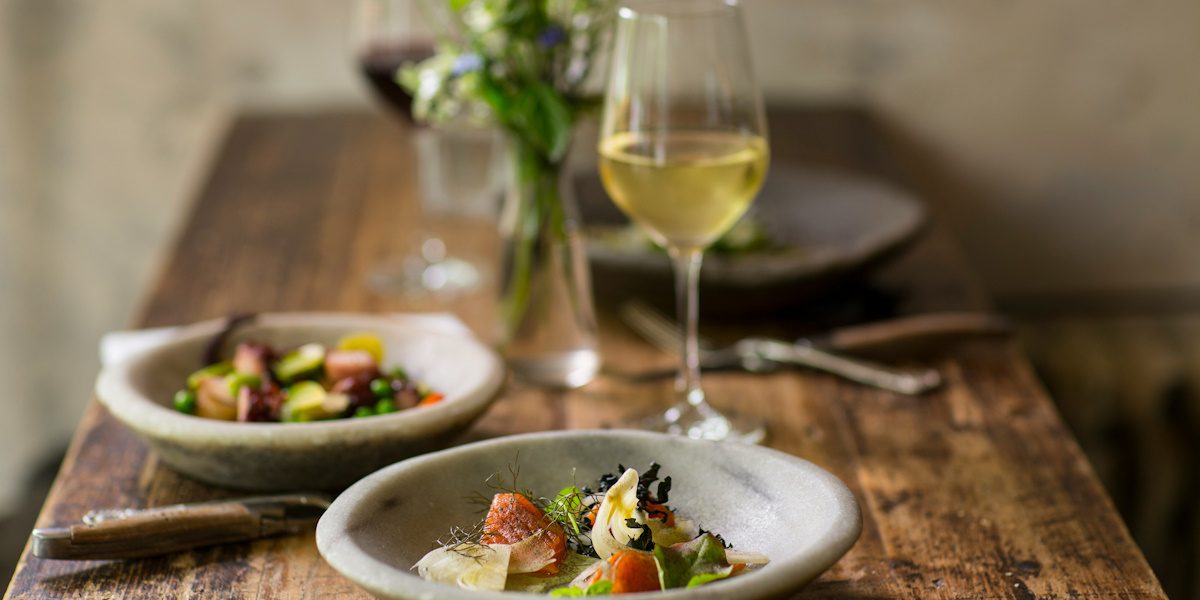 Photo of a wooden restaurant table with two plates of food and a glass of white wine