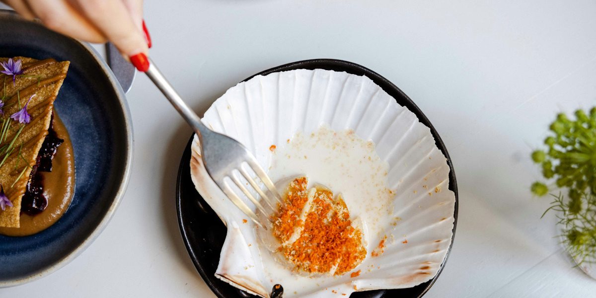 Picture of someone holding a fork and a scallop served in its shell